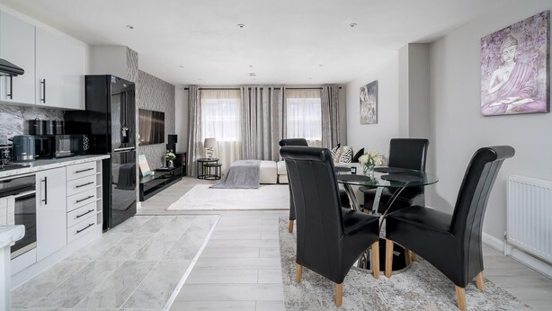 A modern kitchen with a dining area, featuring a black refrigerator, white cabinets, and a dining table with black chairs. - Modern South Wimbledon Stay (London)