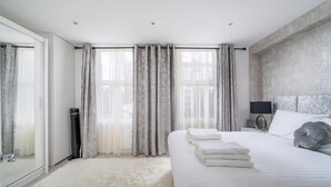 A modern bedroom with a large bed, a bedside table with a lamp, and a wardrobe. - Modern South Wimbledon Stay (London)