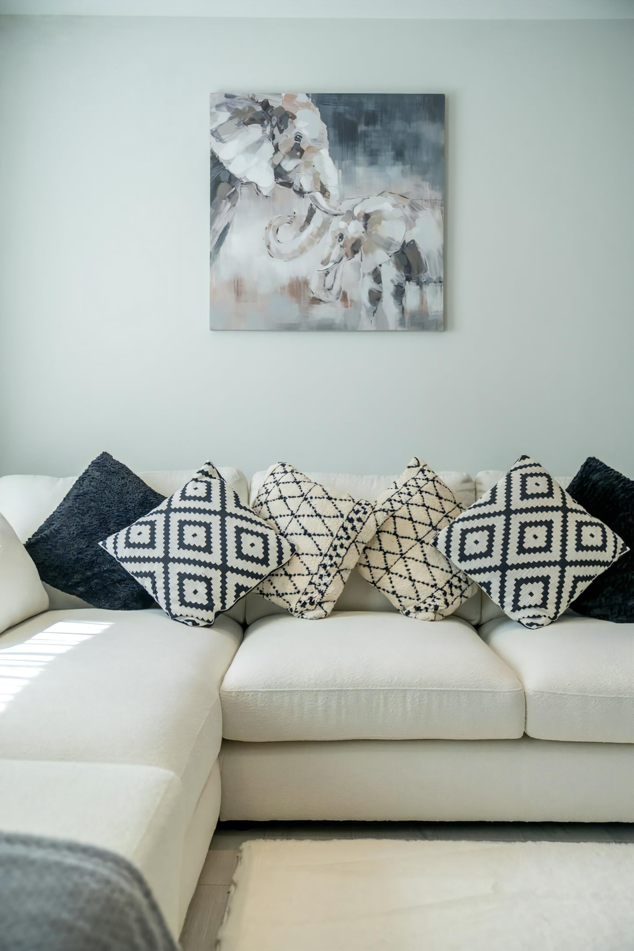 A white sofa with patterned cushions and a painting on the wall.