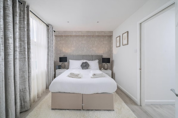 A modern bedroom with a large bed, a headboard, bedside lamps, and a fluffy white rug. - Modern South Wimbledon Stay (London)
