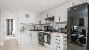 A modern kitchen with white cabinets, a marble backsplash, a Bosch washing machine, and a black refrigerator. - Modern South Wimbledon Stay (London)