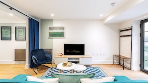 A modern living room with a sofa, a TV, a blue chair, and artwork on the walls. - Cosy and Stylish Studio in the Heart of Greenwich (London)