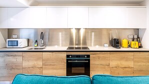 A modern kitchen with white cabinets, a stainless steel range hood, a microwave, a kettle, and a coffee maker. - Cosy and Stylish Studio in the Heart of Greenwich (London)