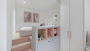 A modern bedroom with a bed, a wardrobe, and a desk area with shelves. - Stylish Earl's Court Studio Plus Patio (London)