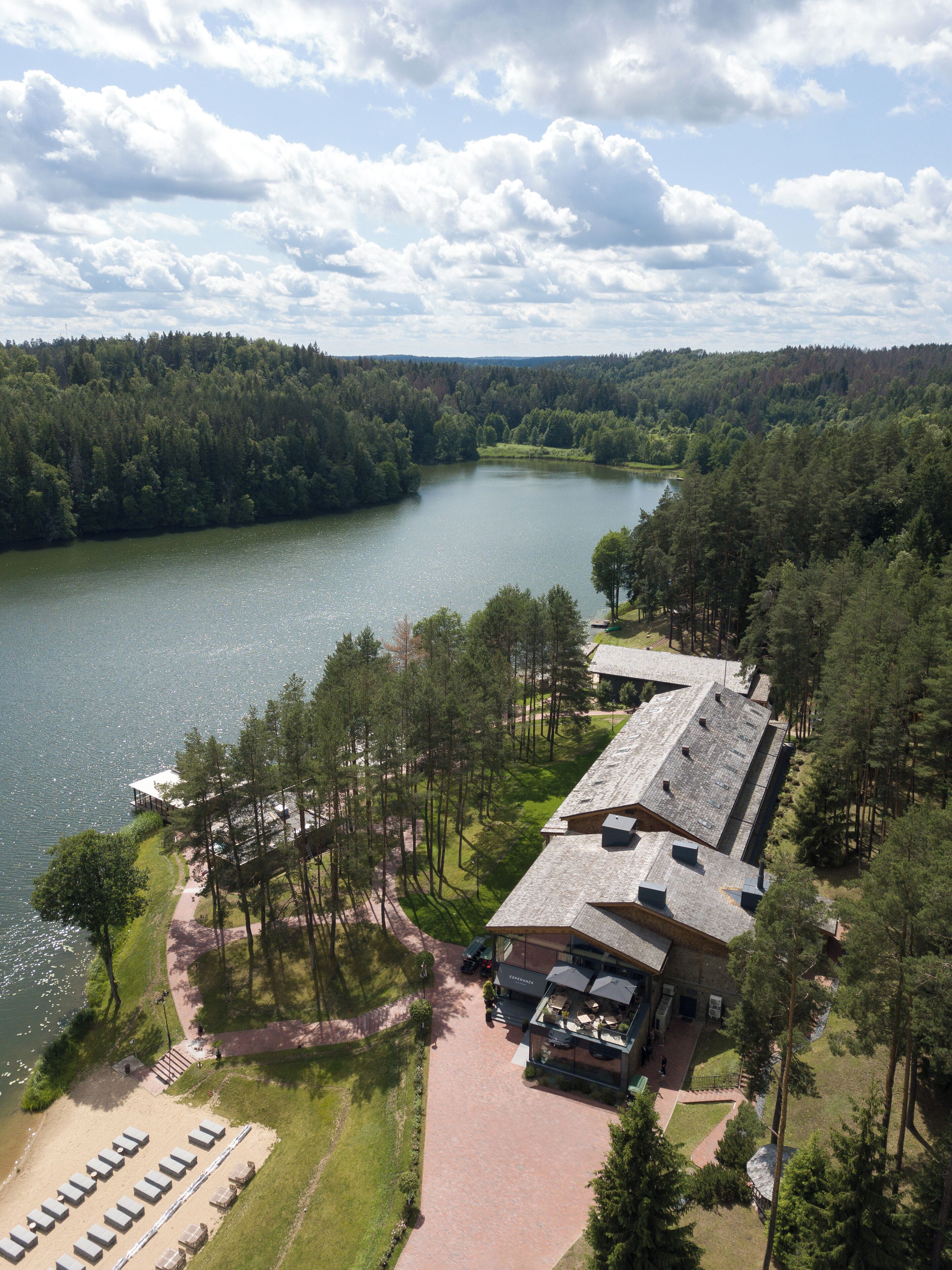 An aerial view of a lakeside lodge with a large deck, a covered outdoor seating area, and a building with a sloped roof.