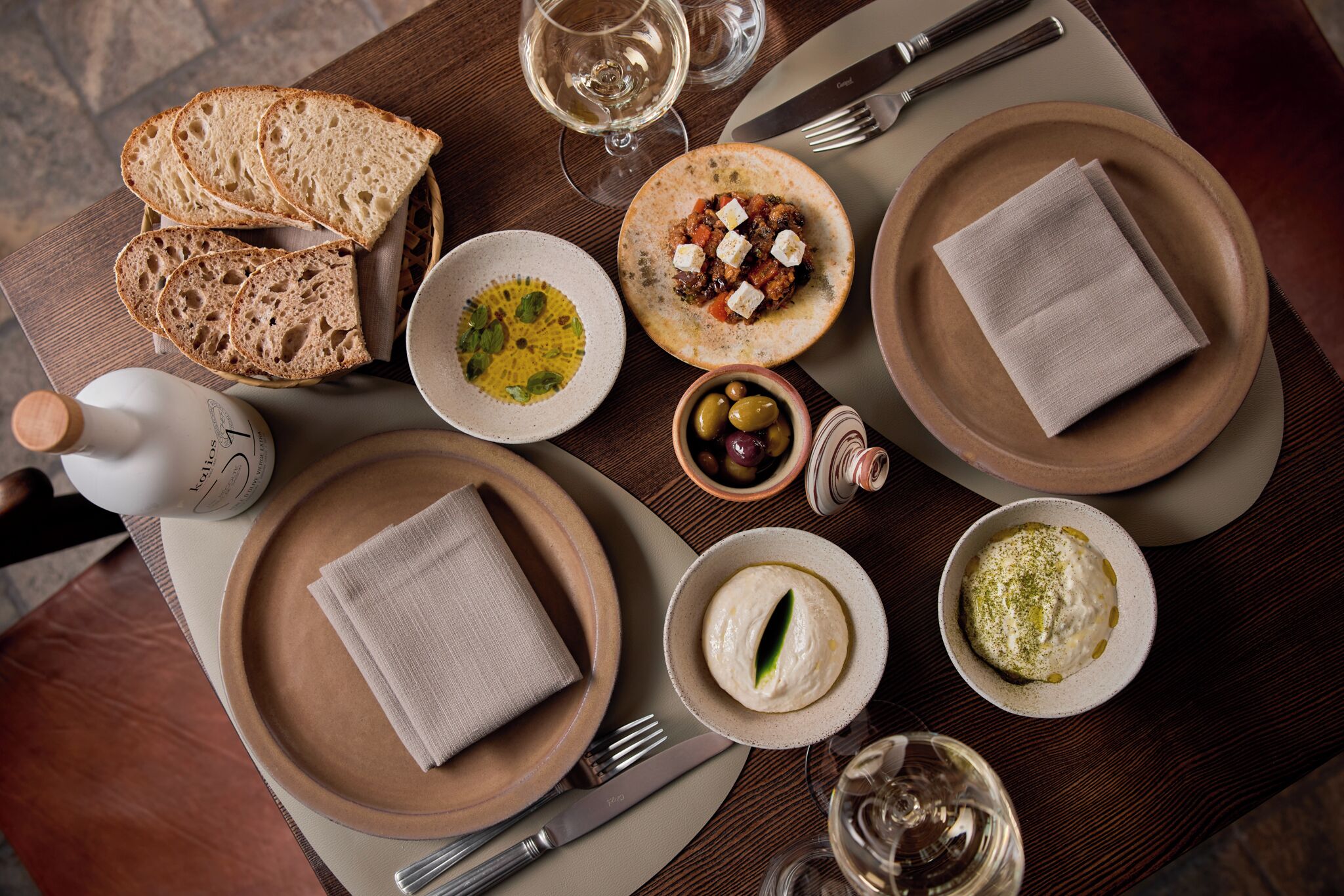 Une table à manger avec du pain, des assiettes de nourriture, des olives et une bouteille d’eau.