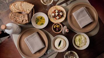 Une table à manger avec du pain, des assiettes de nourriture, des olives et une bouteille d’eau.