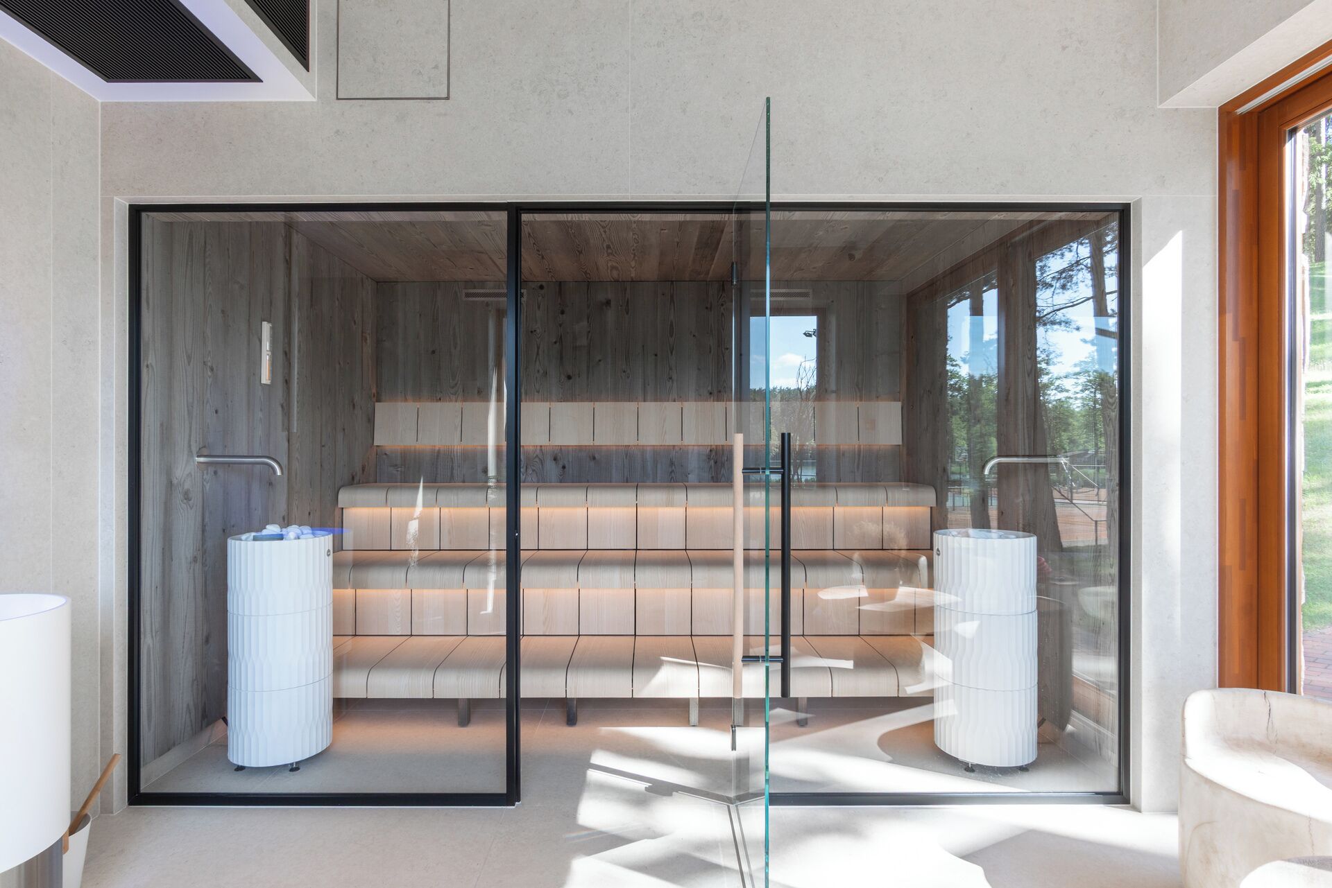 A modern spa room with a glass partition, wooden benches, and a large window offering a view of the outdoors.