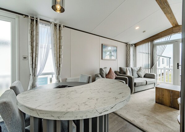 A modern living room with a marble coffee table, grey sofas, and a view of the outside.