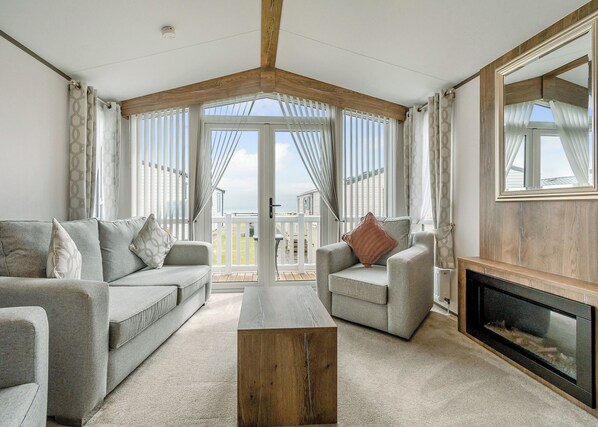 A spacious living room with a high ceiling, a fireplace, and a balcony with a view.