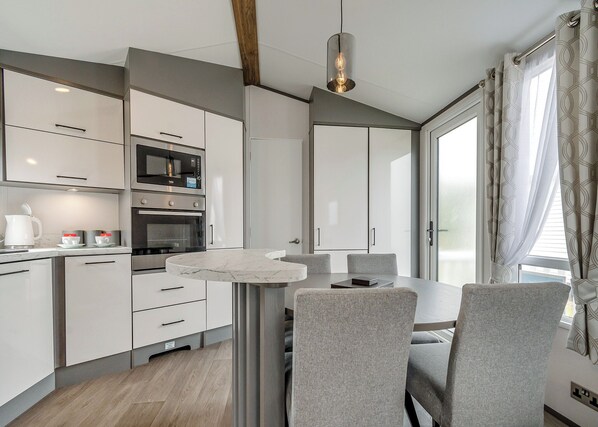 Una cocina moderna con electrodomésticos integrados, una mesa de comedor con sillas y un amplio ventanal con cortinas.