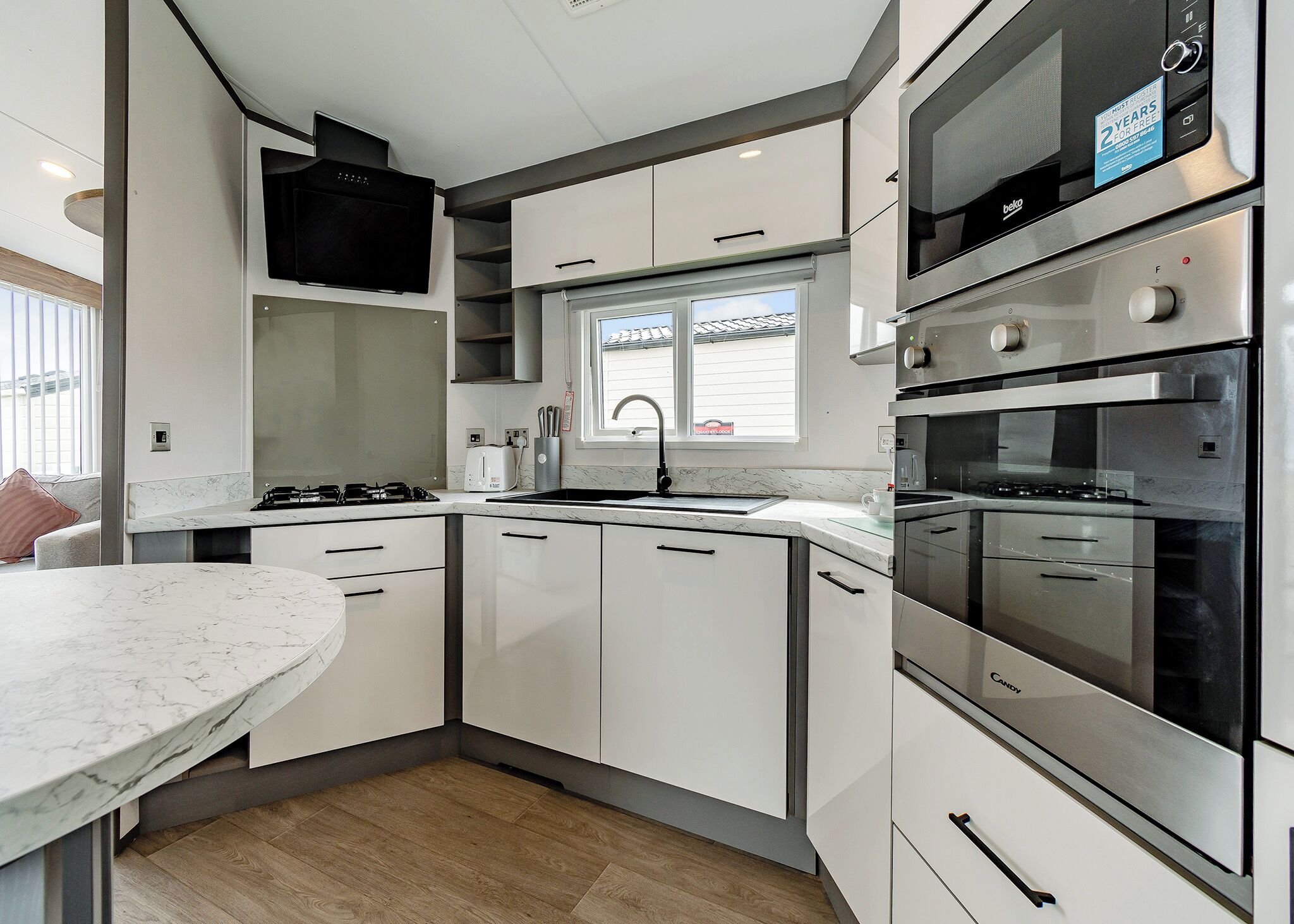 A modern kitchen with white cabinets, a marble countertop, a built-in oven, and a window above the sink.