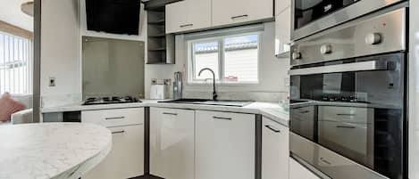 A modern kitchen with white cabinets, a marble countertop, a built-in oven, and a window above the sink.