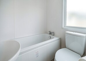 Un baño con una bañera blanca, un inodoro y una ventana.