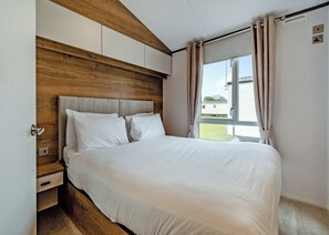 Un dormitorio con cabecera de madera, cama grande, ventana con cortinas y vistas al exterior.