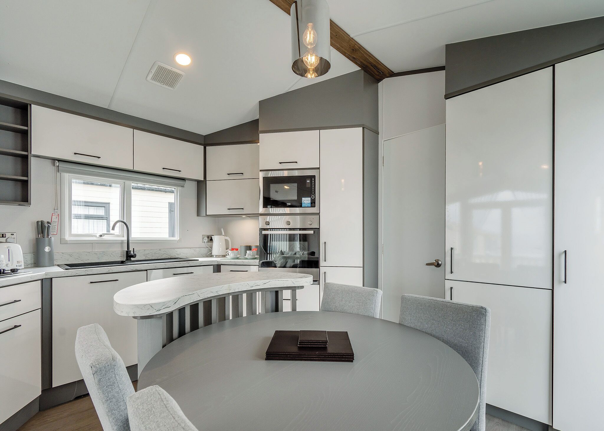 A modern kitchen with white cabinetry, a round dining table, and a built-in oven.