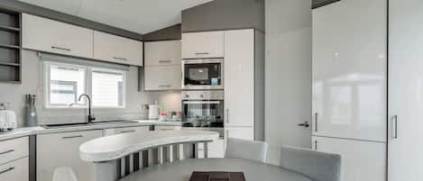 A modern kitchen with white cabinetry, a round dining table, and a built-in oven.
