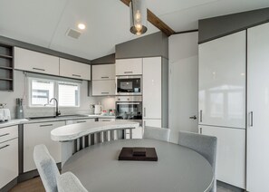A modern kitchen with white cabinetry, a round dining table, and a built-in oven. - 2 bedroom accommodation in Hornsea (Hornsea)