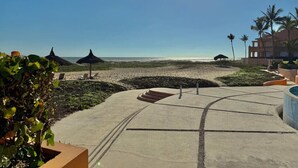 A beachfront resort with a concrete pathway leading to the beach, palm trees, and beach umbrellas. - Depa in EDM first floor beachfront By GPS (Mazatlán)