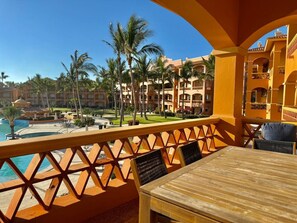 Ein Balkon mit Holztisch und Stühlen mit Blick auf einen Pool und Palmen.