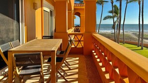 Un balcone con tavolo e sedie di legno, vista su una spiaggia e palme.