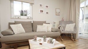 A living room with a sofa, a rocking chair, a coffee table with plants, and a window with blinds.