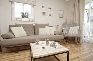 A living room with a sofa, a rocking chair, a coffee table with plants, and a window with blinds. - Vacation apartment in Göhren with free use of the swimming pool in Sellin - Villa Karola (Göhren (Ostseebad))