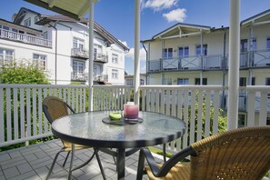 En balkon med et rundt glasbord, fletstole og et hvidt hegn med spindler.