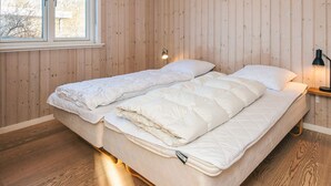 A bedroom with a wooden wall, a bed with white bedding, a nightstand with a lamp, and a window with a view of trees. - 4 Star Holiday Home in Hemmet (Hemmet)