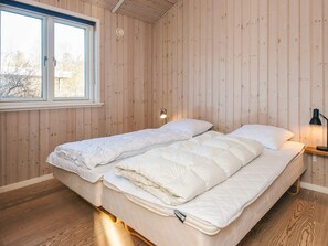 A bedroom with a wooden wall, a bed with white bedding, a nightstand with a lamp, and a window with a view of trees. - 4 Star Holiday Home in Hemmet (Hemmet)