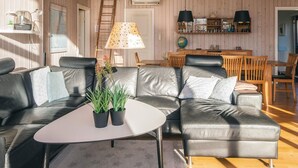 A modern living room with a leather sofa, a small white table, and a wooden dining area with chairs. - 4 Star Holiday Home in Hemmet (Hemmet)