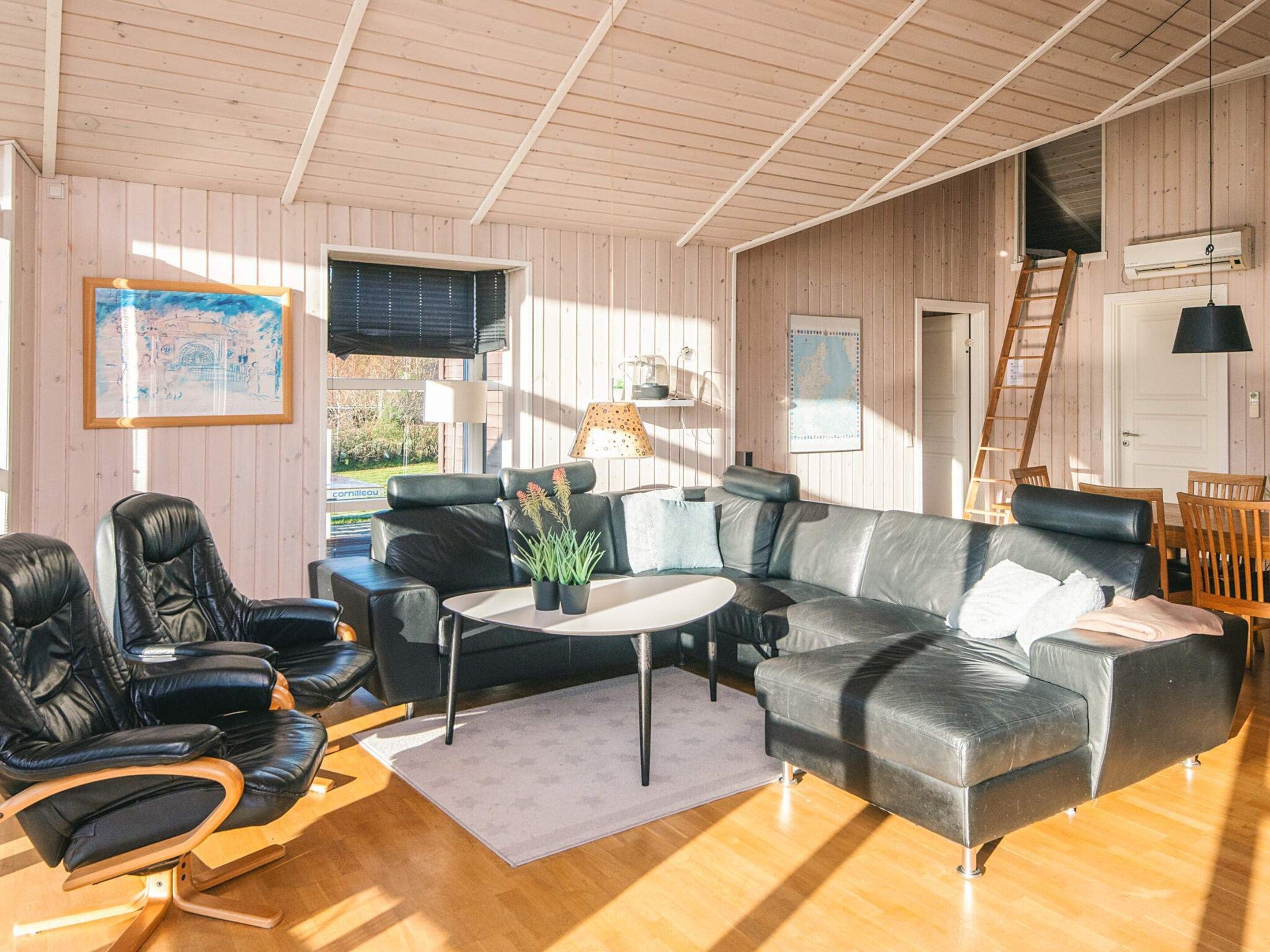 A cozy living room with a leather sofa, black chairs, a coffee table, and a wooden floor.