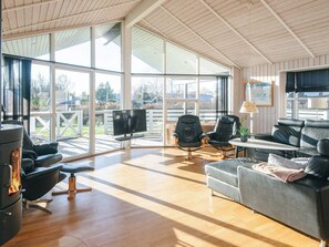 A spacious living room with a fireplace, comfortable seating, a television, and large windows offering a view of the outdoors. - 4 Star Holiday Home in Hemmet (Hemmet)