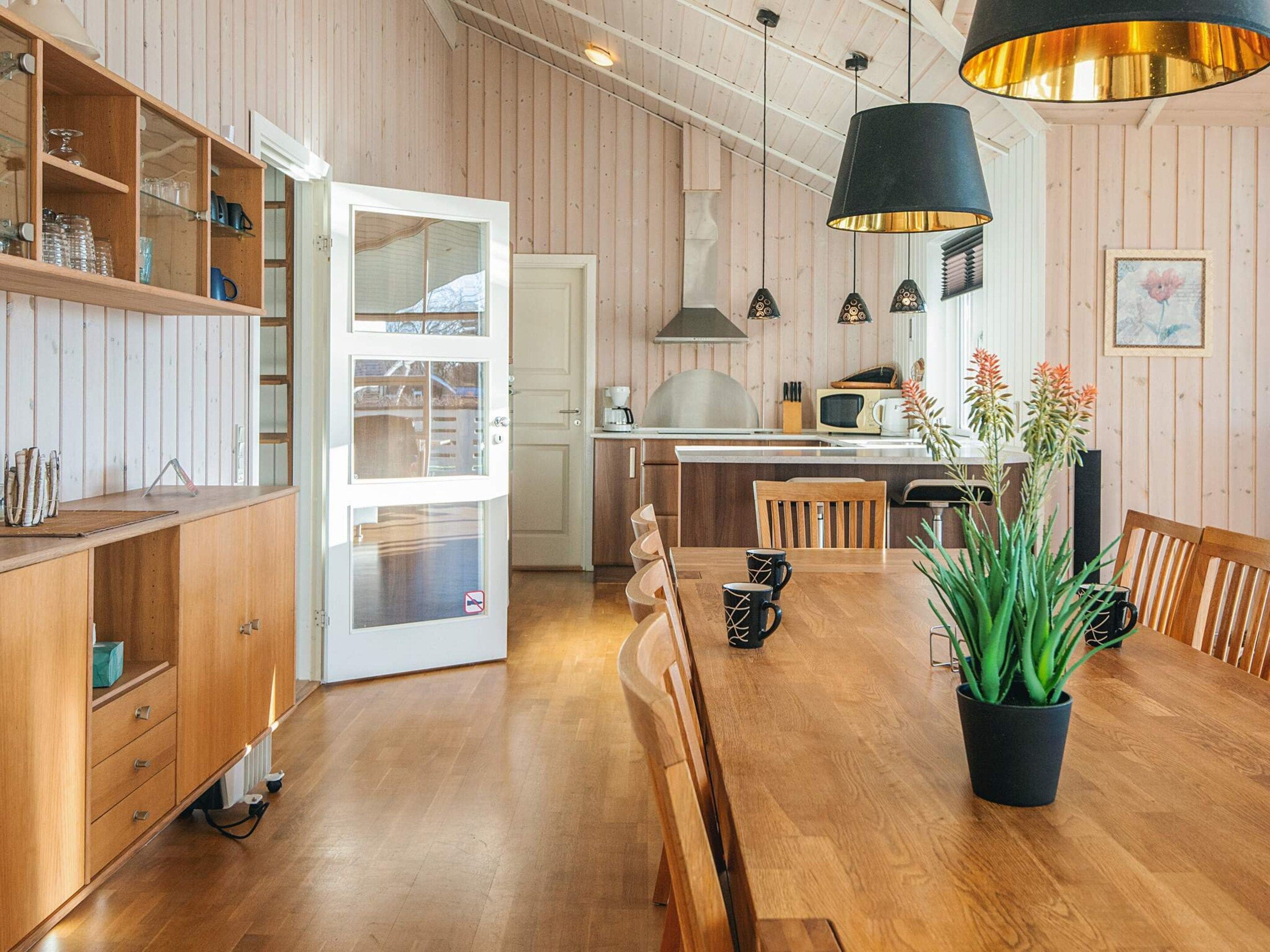 Eine moderne Küche mit Holzschränken, einem Esstisch mit Stühlen und Pendelleuchten.