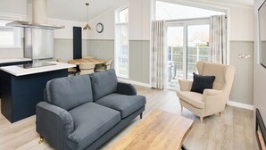 En moderne stue med sofa, sofabord, spiseområde med bord og stole, samt et køkken med komfur og en hængende lampe.