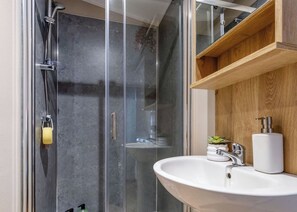 A modern bathroom with a glass shower enclosure, a white sink, and a wooden shelf.