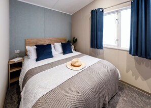 A neatly made bed with a white and gray blanket, a beige hat, and blue pillows.