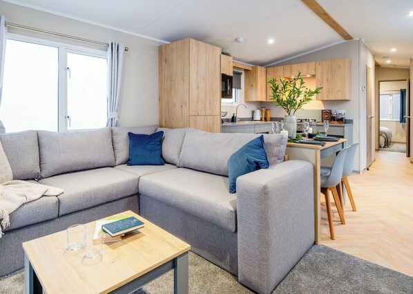 A modern living room with a grey sectional sofa, a wooden coffee table, and a dining area with a wooden table and chairs.