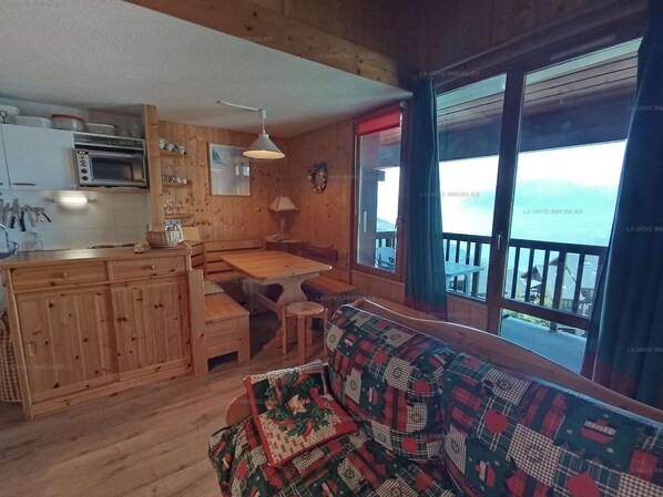 Interior acogedor de una cabaña con zona de comedor de madera, kitchenette y un amplio ventanal con vistas.
