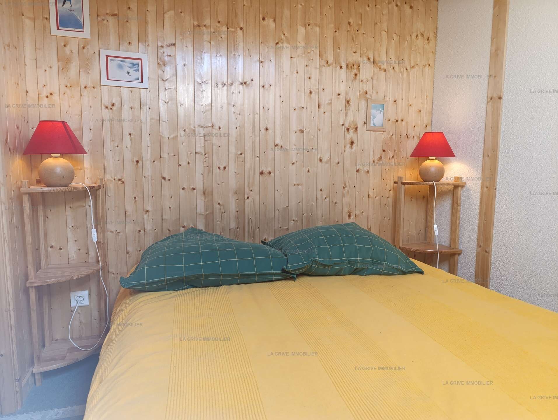 A room with a wooden paneled wall, two bedside lamps, a bed with green pillows, and a yellow bedspread.
