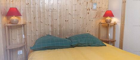 A room with a wooden paneled wall, two bedside lamps, a bed with green pillows, and a yellow bedspread.
