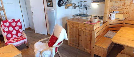 A cozy kitchen with wooden cabinets, a dining table, and a chair with a red cushion.