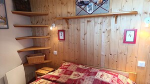 Et værelse med træpaneler, en seng, reoler og en lampe monteret på væggen.