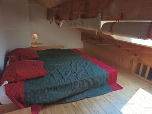 Un dormitorio con techo de madera, una cama con colcha estampada, una lámpara de noche y una ventana con vistas.