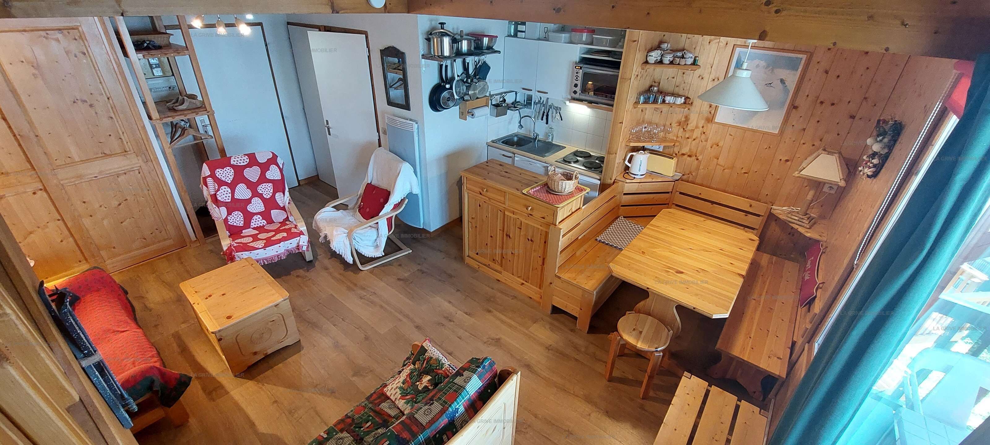 Quarto compacto com cozinha americana, área de estar com uma cadeira de madeira com padrão de coração vermelho e mesa de jantar de madeira.
