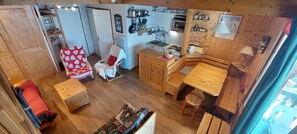 Una habitación compacta con kitchenette, un área de estar con una silla de estampado de corazón rojo y una mesa de comedor de madera.
