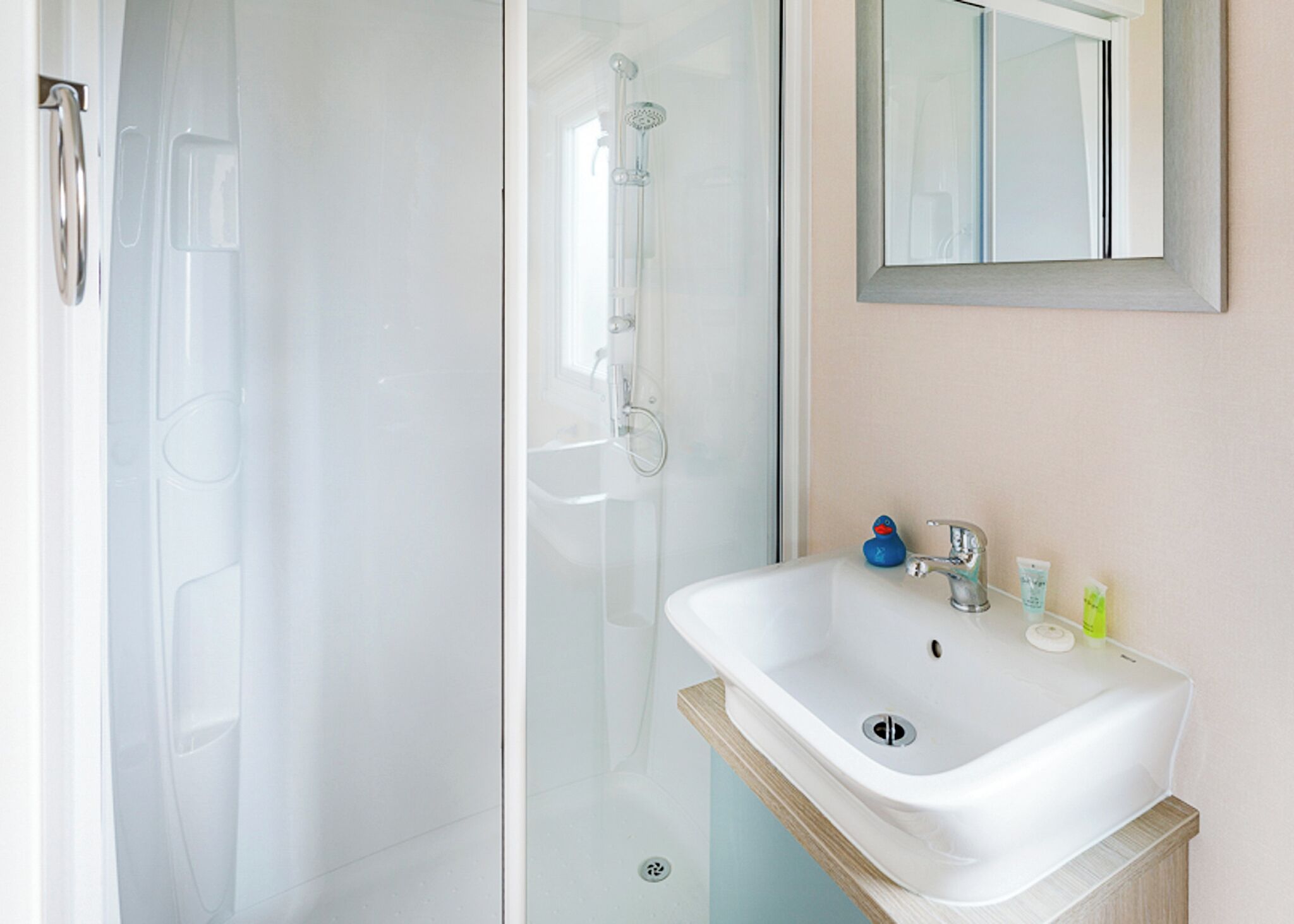 A bathroom with a glass shower enclosure, a white sink with a wooden countertop, and a mirror above the sink.
