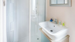 A bathroom with a glass shower enclosure, a white sink with a wooden countertop, and a mirror above the sink.