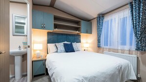 A bedroom with a bed, bedside lamps, a window with curtains, a radiator, and a built-in shelf above the bed.