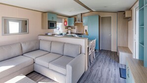 A modern RV interior with a sofa, kitchenette, and a door leading to a bathroom.